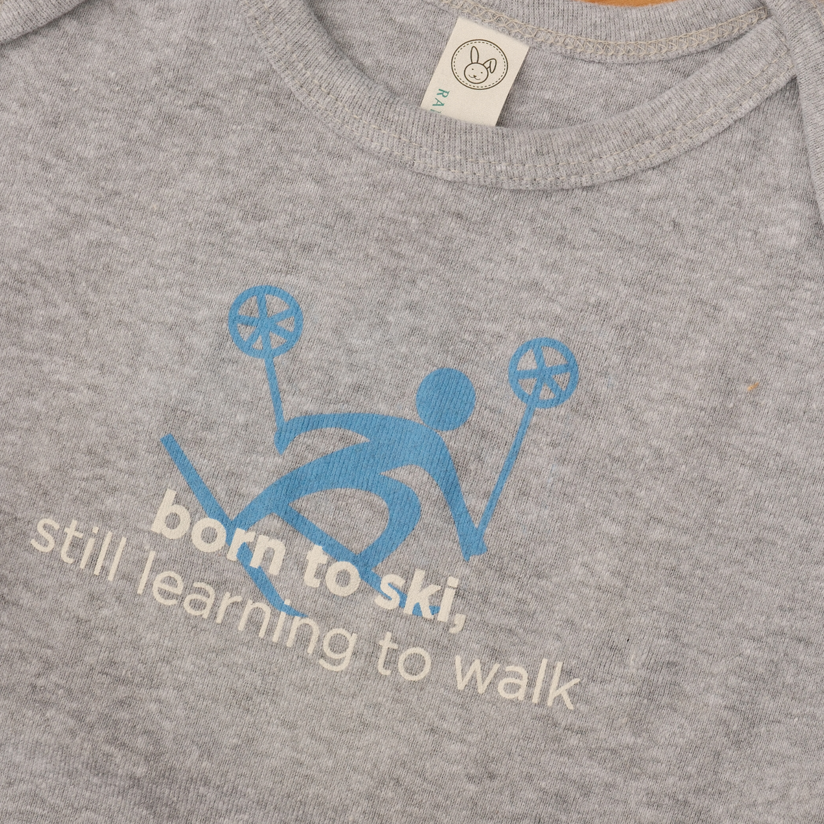 Grey baby onesie with a blue skier graphic and ‘born to ski. still learning to walk’ lettering.