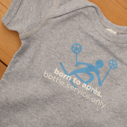 Grey baby onesie with a blue skier graphic and ‘born to après. bottle service only’ lettering.