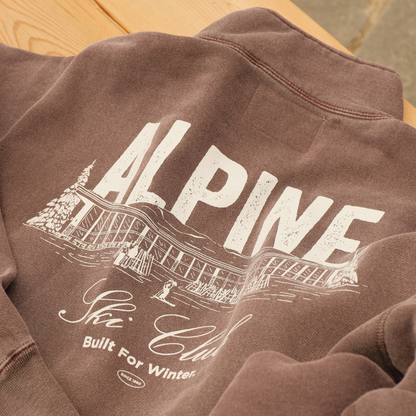Plum Alpine Ski Club quarter-zip sweater showing its white chalet back graphic and ‘Built For Winter’ slogan.