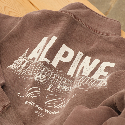 Plum Alpine Ski Club quarter-zip sweater showing its white chalet back graphic and ‘Built For Winter’ slogan.