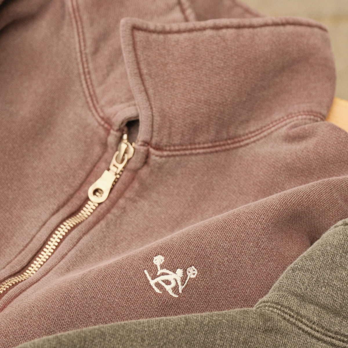 Close-up of the plum Alpine Ski Club quarter-zip’s metal zipper, stand collar and white embroidered skier chest logo.