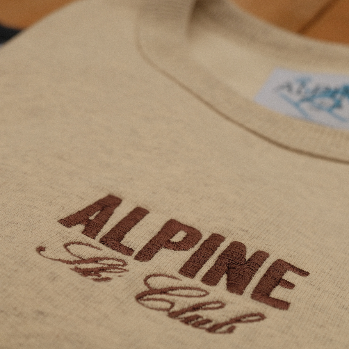 Close-up of burgundy Alpine Ski Club chest embroidery on a cream crewneck sweatshirt.