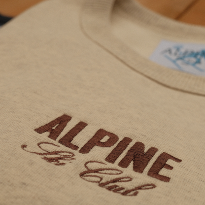 Close-up of burgundy Alpine Ski Club chest embroidery on a cream crewneck sweatshirt.