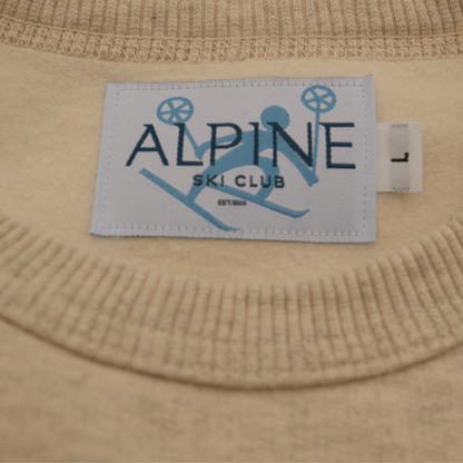 Close-up of the Alpine Ski Club neck label and ribbed collar on a cream crewneck sweatshirt.