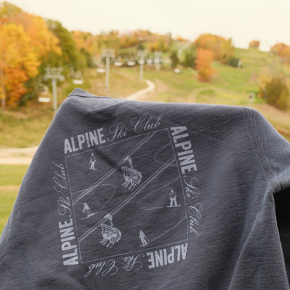 Navy Alpine Ski Club crewneck showing its skier and chairlift back graphic against an autumn ski hill.