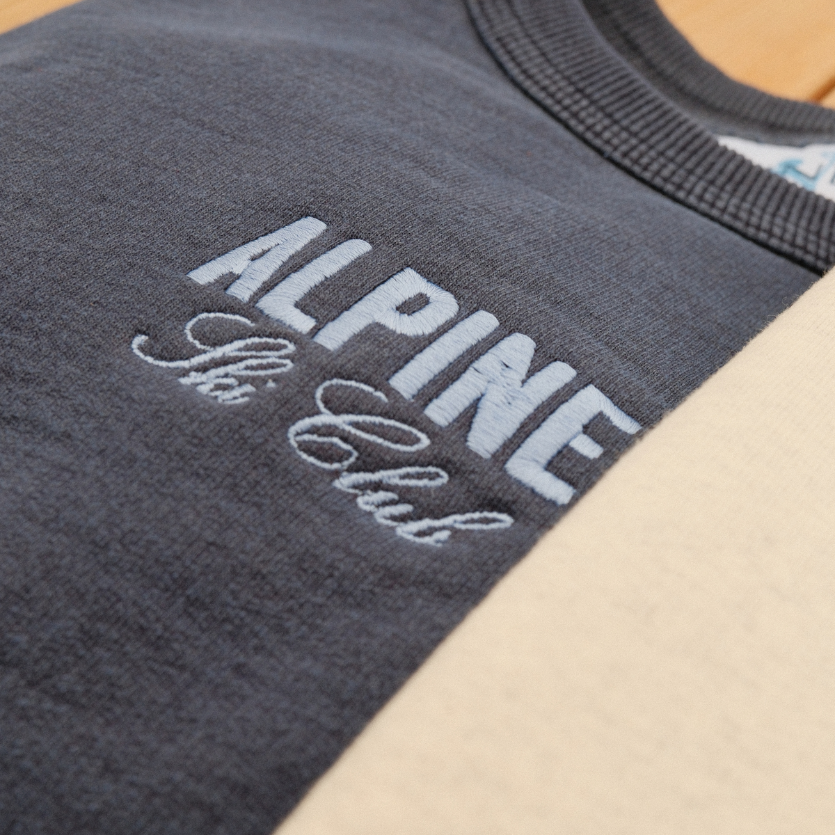 Close-up of light blue Alpine Ski Club chest embroidery on a navy crewneck sweatshirt.