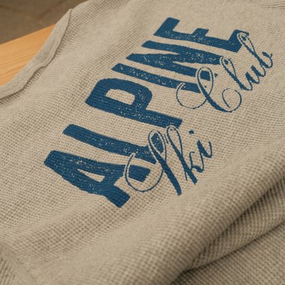 Close-up of distressed blue ‘Alpine Ski Club’ lettering on a light grey waffle-knit Henley.
