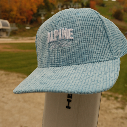 Carolina blue corduroy Alpine Ski Club dad hat with white embroidered lettering, shown outdoors.
