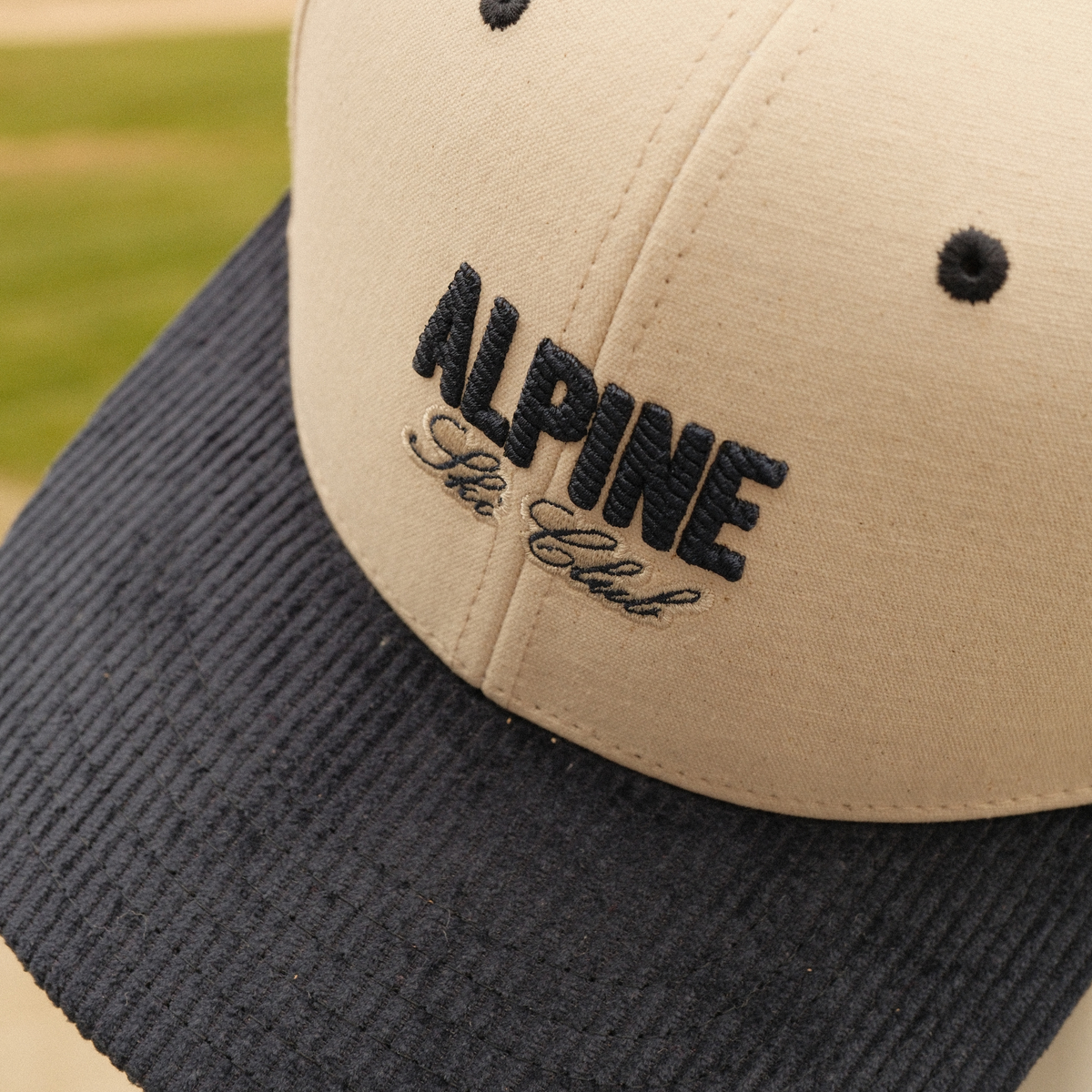 Close-up of cream Alpine Ski Club dad hat with navy embroidered lettering and a navy corduroy brim.